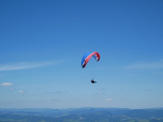 Fototapeta na wymiar Carpathians / Ukraine - July 07 2017: Paraglider flying parachute in blue sky at a bright sunny summer day. Active lifestyle
