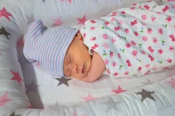 Sleeping newborn caucasian baby with hat. Little child wrapped in cotton blanket.