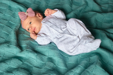 Newborn baby girl with bow in white footed pajamas. Top view. Child on green wool clothes.