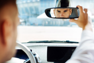 Professional driving. Confident smart man looking into the rearview mirror while driving his car