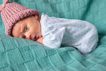 Newborn surprised baby girl in bed. Warm winter clothes, pink woolen hat.