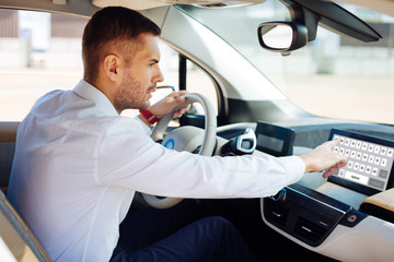 Modern gadget. Confident handsome man typing on the tablet while sitting behind the wheel