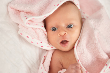 Portrait of newborn baby face with opened mouth. Covered with pink blanket. Close up.