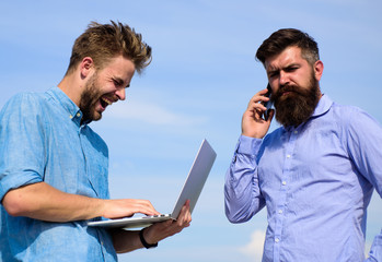 Business team works outdoor, sky background. Men with laptop and smartphone solving problems using...