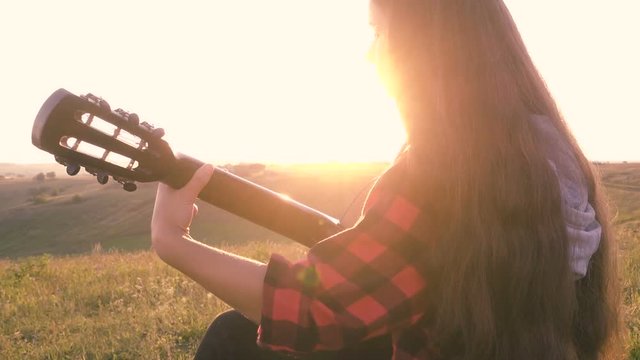 Young girl playing guitar on meadow at the sunset