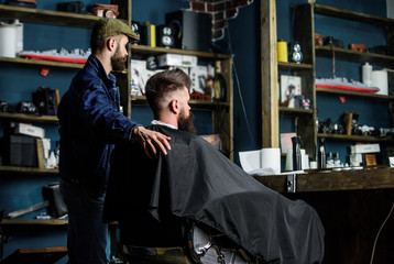 Hipster client got new haircut. Barber with bearded man looking at mirror, barbershop background. Haircut concept. Client and professional master checking result. Barber finished trimming