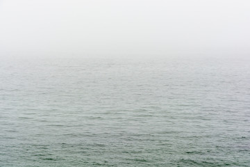 Flat grey sea with wavelets disappearing in the fog.