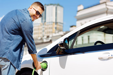 Fuel refilling. Joyful handsome man holding a fuel nozzle while refilling his car