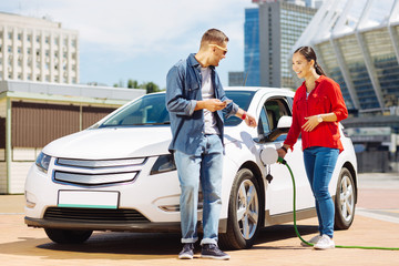 Pleasant interaction. Happy nice woman talking to her male friend while fuelling the car