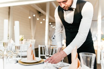 Waiter man serving Cutlery on the tables in the restaurant to prepare for the reception of visitors placing glasses