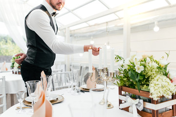 Waiter man in uniform lights candles on the table