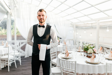 Waiter man in uniform holding a towel in his hand standing in a restaurant with a panoramic roof