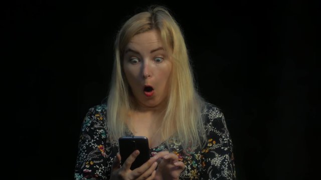 Shocked blond pretty girl looks mobile phone news in the dark