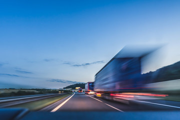 Background photograph of a highway. Truck on a motorway, motion blur, light trails. Evening or night shot of trucks doing logistics and transportation on a highway. - obrazy, fototapety, plakaty