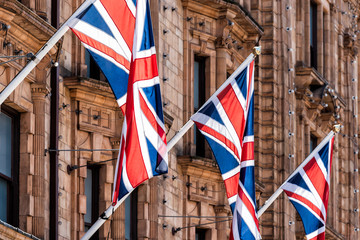 Closeup of row of national flags hanging in London, UK, United Kingdom, Great Britain on wall of building, poles historic architecture