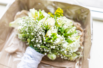 Wedding bouquet in cardboard box on sunny windowsill window sill during morning day lying in room of hotel, many flowers, green yellow lily