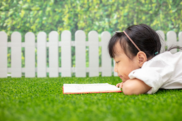 Asian Little Chinese girl kneeling on the grass and reading book