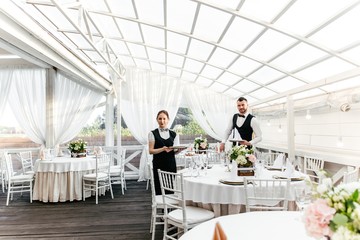 Two waiters, a man and a woman, will serve a round table in the restaurant in preparation for the...