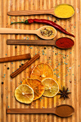 Culinary arts concept. Spices scattered around cutting board. Spoon filled with cinnamon, grinded red pepper and curcuma powder lay on cutting board. Spoon with spices on wooden texture