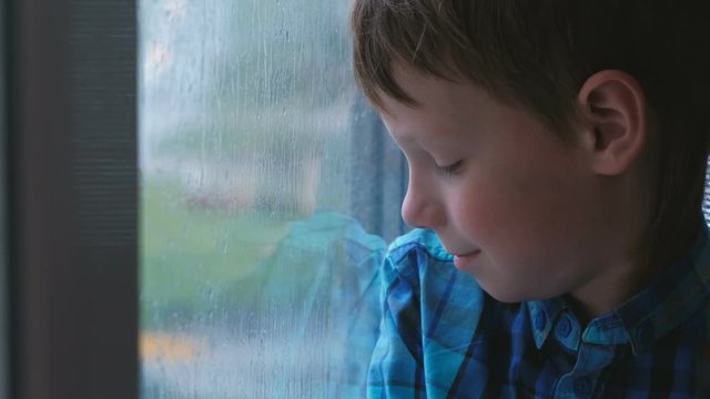 Boy looks out the window in the rain and is sad.