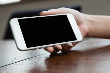 Mockup image of a woman holding and showing white mobile phone with blank black screen for watching on wooden table
