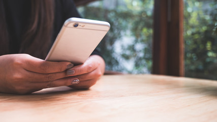 Closeup image of a woman holding , using and looking at smart phone with blur green nature background