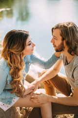 Stylish young couple. Film photo with a light and a sunlight. The guy with a stylish haircut, and with hair on his shoulders hugs a red-haired girl. Background stones and river