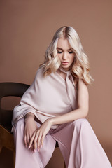 Sexy luxurious woman in a dress sitting on a chair. Autumn collection of women clothing. Fashion blonde in a long beautiful dress posing on background. Beautiful hair and a perfect girl figure