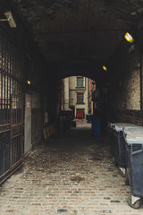 Fototapeta na wymiar Dark and old alley. Creepy passage with trash bins, windows and surveillance camera. Urban scene of Leeds, England, UK.