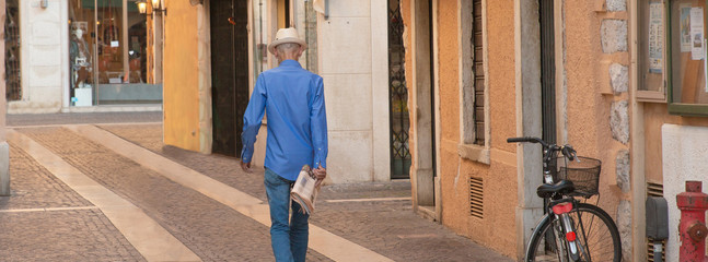 älterer Mann mit Zeitung und Hut auf dem Weg ins Café