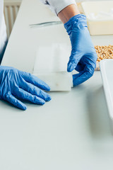 cropped image of biologist in latex gloves working at table with seeds in agro laboratory