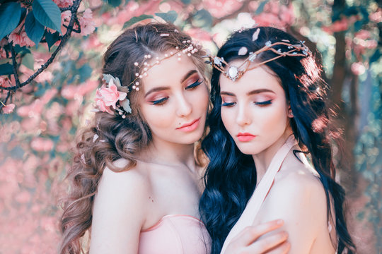 Two amazing elves with a gentle spring makeup close-up. Blonde and brunette with long, healthy, wavy hair. Handmade diadem decoration. Portrait photo. Background of a blooming sakura garden