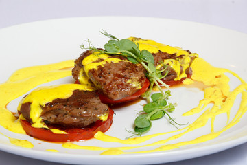 Slices of the fried meat on the lobules of tomatoes with greenery and sauce on a white dish