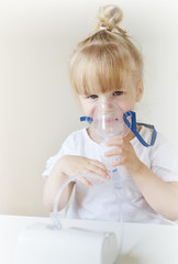 Little girl in a mask for inhalations, making inhalation with nebulizer at home inhaler on the table, indoor, sick child