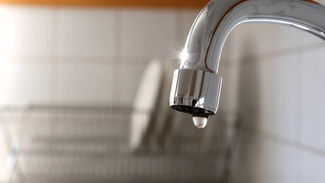 Water drops slowly falling from kitchen tap, dish dryer rack with plates on background, 4k
