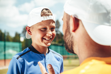 Beaming child expressing gladness while speaking with coach on field. He gesticulating hand
