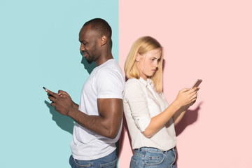 Mixed raced couple of students taking mobile phones. Caucasian girl and her African boyfriend posing at studio .