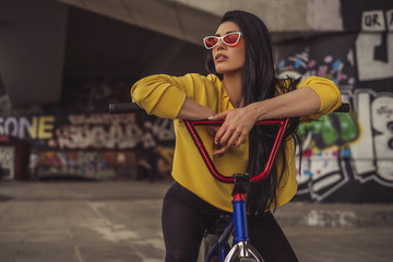 Sexy slim fit brunette woman in sport casual outfit in a skate park. Active leisure on a bicycle