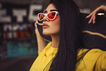 Sexy slim fit brunette woman in sport casual outfit in a skate park. Active leisure on a longboard