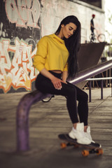 Sexy slim fit brunette woman in sport casual outfit in a skate park. Active leisure on a longboard