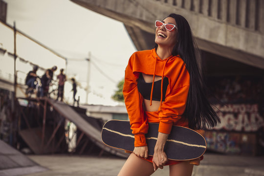 Sexy slim fit brunette woman in sport casual outfit in a skate park. Active leisure on a longboard