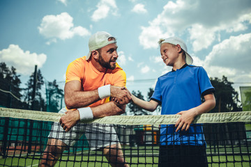 Side view beaming man shaking hand of smiling kid during conversation after workout on field
