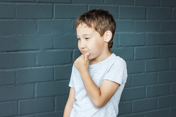 Boy 8 years old with freckles looking into the distance, thinking and scratching his head against the gray brick wall