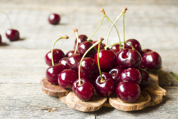 Juicy ripe cherries with twigs on wooden stand on rustic background.