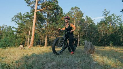 Fat bike also called fatbike or fat-tire bike in summer riding in the forest. Beautiful girl and her bicycle in the forest. She poses and smiles to the operator. Very positive and provocative.