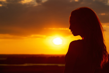 silhouette of a beautiful girl at sunset in a field, face profile of young woman