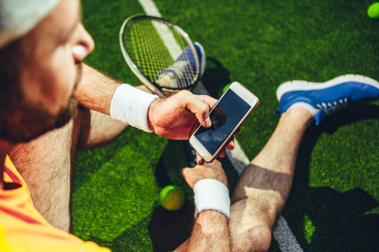 Calm male athlete looking at screen of mobile while resting after hard game in tennis