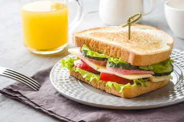 Sandwich with cheese, ham and fresh vegetables on a plate. Fresh juice and a Cup of coffee. The concept of Breakfast.