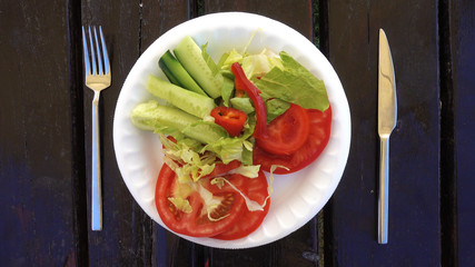 A salad of fresh vegetables rotates on a white plate. Wooden table. Salad of tomatoes and cucumbers is spinning.