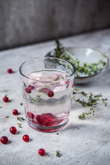 A simple glass on a gray background with a lemonade of cranberries and thyme